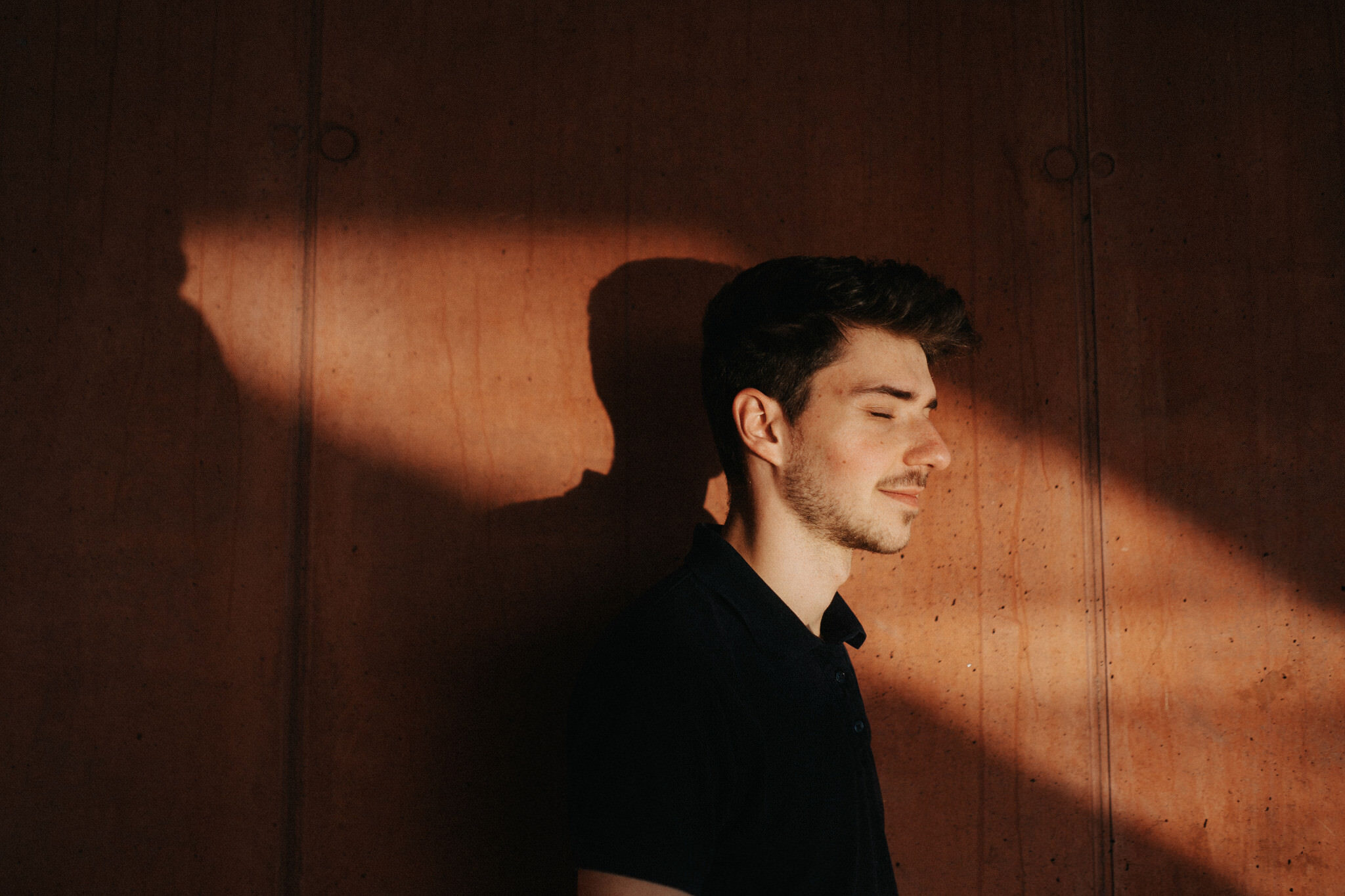 a man with eyes closed standing in front of a wall